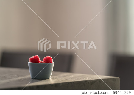 Fresh ripe raspberries in small blue bowl on concrete countertop 69451799