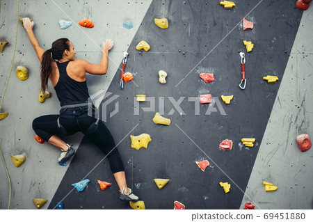 Woman practicing rock climbing on artificial wall indoors. Active lifestyle and bouldering concept. Woman practicing rock climbing on artificial wall indoors. Active lifestyle and bouldering concept. 69451880