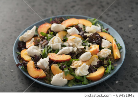 salad with nectarines, mozzarella and mixed greens in blue plate on concrete background 69451942