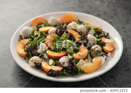 Closeup salad with nectarines, mozzarella and mixed greens in white plate on concrete background 69451972