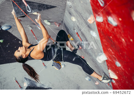 Woman reaching the top of artificial bouldering wall while exercising in gym. Woman reaching the top of artificial bouldering wall while exercising in gym. 69452672