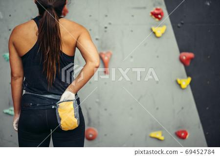 Rear view climber woman rubbing hands with chalk powder from a bag on her waist. Rear view climber woman rubbing hands with chalk powder from a bag on her waist. 69452784