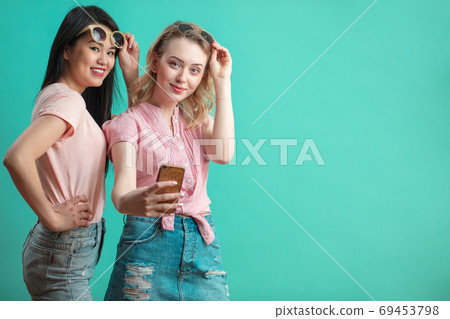happy diverse young girls taking selfie with smartphone against blue wall 69453798