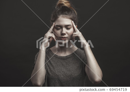 Studio shot of concentrated young Caucasian woman holding fingers on her temples Studio shot of concentrated young Caucasian woman holding fingers on her temples 69454719