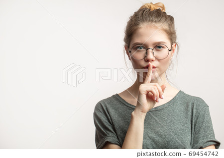 Caucasian woman with hair bun keeping index finger at lips, isolated over white. Caucasian woman with hair bun keeping index finger at lips, isolated over white. 69454742