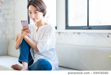 Middle-aged woman operating a smartphone in the living room Middle-aged woman operating a smartphone in the living room 69456080