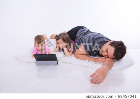 the kids are watching cartoons on the tablet. a man sleeps. Family vacation, joint pastime. Parents with girls on the floor 69457041