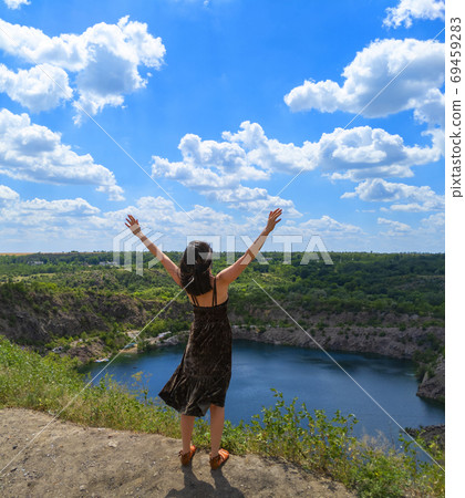 A young woman with open hands up stands on a hill above a picturesque lake. Freedom concept. Stock photo. A young woman with open hands up stands on a hill above a picturesque lake. Freedom concept. Stock photo. 69459283