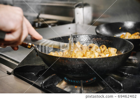 Chef cooking mushrooms in frying pan on burning fire. Chef cooking mushrooms in frying pan on burning fire. 69462402