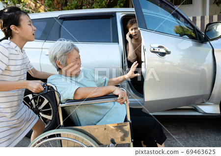 Asian female people enjoy talking on the phone,opening the door car slamming the leg of elderly feel pain, inattentive girl crashed into leg of disabled senior woman in wheelchair while open the door 69463625