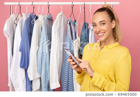 Happy woman holding phone standing near rack with clothing Happy woman holding phone standing near rack with clothing 69465000