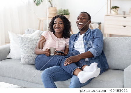 Joyful african man and woman drinking tea and watching movie Joyful african man and woman drinking tea and watching movie 69465051