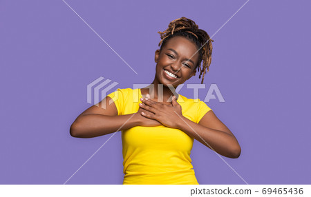 Thankful smiling african girl holding hands on her chest Thankful smiling african girl holding hands on her chest 69465436