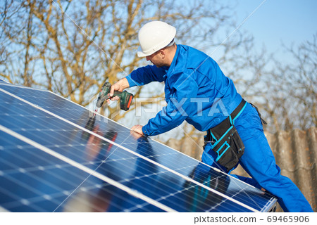 Electrician mounting solar panel on roof of modern house 69465906