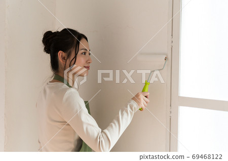 A woman who paints the walls of a house with DIY 69468122