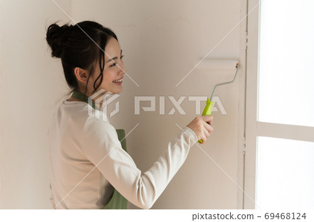 A woman who paints the walls of a house with DIY 69468124