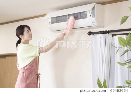 A woman wiping the air conditioner with a handy mop 69468664