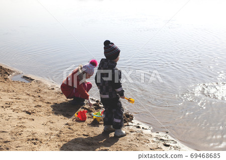 Two children are playing on the beach near the river. 69468685