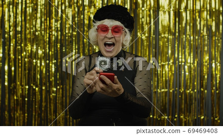 Shocked happy senior old woman with mobile phone. Shouting, celebrating success, winning lottery Shocked happy senior old woman with mobile phone. Shouting, celebrating success, winning lottery 69469408