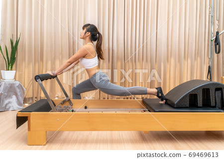 Young Asian woman working on pilates reformer machine Young Asian woman working on pilates reformer machine 69469613