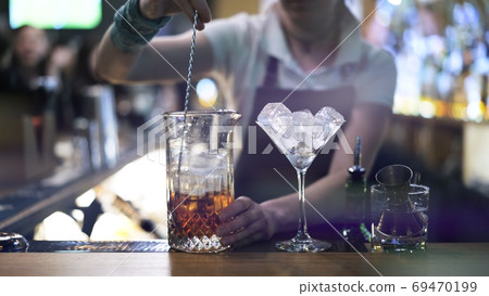 Alcohol mixing with cubes of ice on background of barman at bar Alcohol mixing with cubes of ice on background of barman at bar 69470199