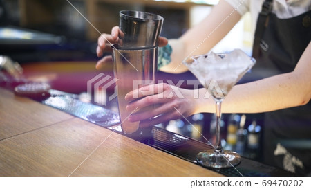 Metal cups on bar counter, bartender taking cups to mix cocktail, lens flare Metal cups on bar counter, bartender taking cups to mix cocktail, lens flare 69470202