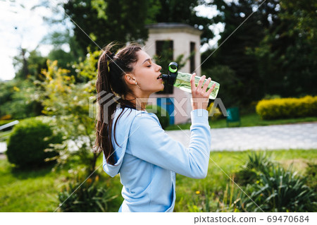 Young woman in a sporting suit drinks from a bottle after a workout Young woman in a sporting suit drinks from a bottle after a workout 69470684