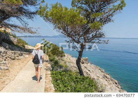 Young active feamle tourist wearing small backpack walking on coastal path among pine trees looking for remote cove to swim alone in peace on seaside in Croatia. Travel and adventure concept 69470877