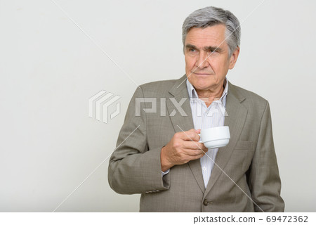 Portrait of handsome senior businessman thinking while holding coffee cup 69472362
