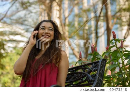Happy young beautiful Indian woman talking on the phone at the park 69473248