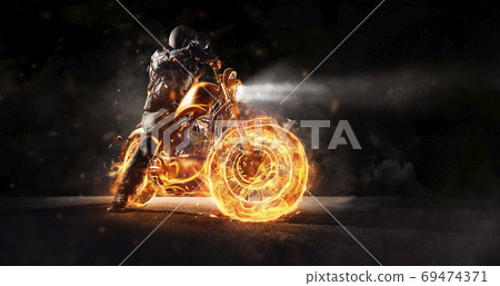 Dark motorbiker staying on burning motorcycle at night. 69474371