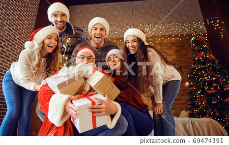 Friends in Santa's hats change gifts at the Christmas party Friends in Santa's hats change gifts at the Christmas party 69474391