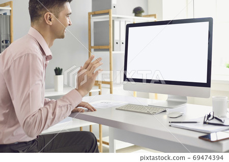 Man using personal desktop computer for teleconference and waving hand during video call Man using personal desktop computer for teleconference and waving hand during video call 69474394