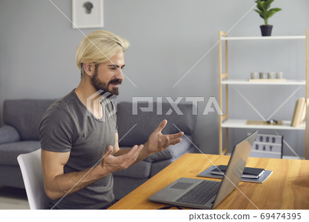 Man sitting at home, looking at laptop screen and smiling during online during meeting Man sitting at home, looking at laptop screen and smiling during online during meeting 69474395
