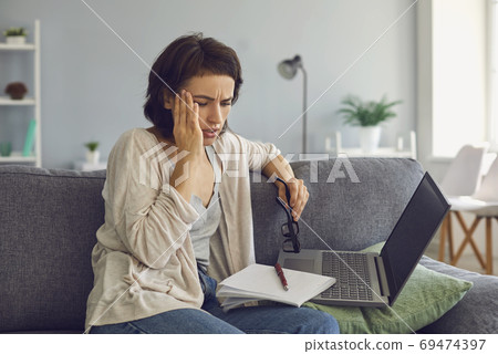 Young stressed woman sitting near laptop and touching temple with hand Young stressed woman sitting near laptop and touching temple with hand 69474397