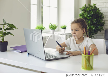 Online schooling. Little girl participating in video lesson on laptop at home. Child taking notes during webinar at home Online schooling. Little girl participating in video lesson on laptop at home. Child taking notes during webinar at home 69474398