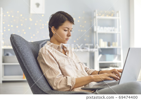 Businesswoman working on personal laptop sitting in comfortable armchair in cozy home office 69474400