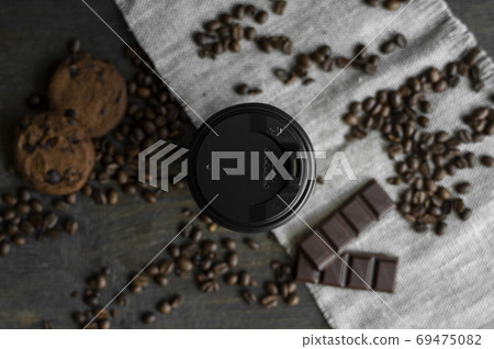 Paper cup of coffee with roasted coffee beans on wooden table. Mug of black coffee with a cookies and chocolate on a table. Paper cup of coffee with roasted coffee beans on wooden table. Mug of black coffee with a cookies and chocolate on a table. 69475082
