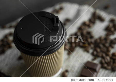Paper cup of coffee with roasted coffee beans on wooden table. Mug of black coffee with a cookies and chocolate on a table. Paper cup of coffee with roasted coffee beans on wooden table. Mug of black coffee with a cookies and chocolate on a table. 69475095