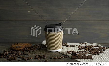 Paper cup of coffee with roasted coffee beans on wooden table. Mug of black coffee with a cookies and chocolate on a table. Paper cup of coffee with roasted coffee beans on wooden table. Mug of black coffee with a cookies and chocolate on a table. 69475122