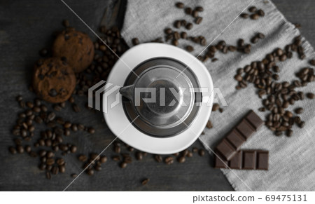 White cup of coffee with a metal filter on a top and scattered beans on a wooden table. Traditional vietnamese coffee. 69475131