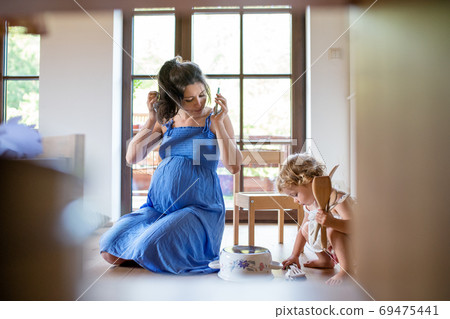 Pregnant woman with small child indoors at home, using smartphone. Pregnant woman with small child indoors at home, using smartphone. 69475441