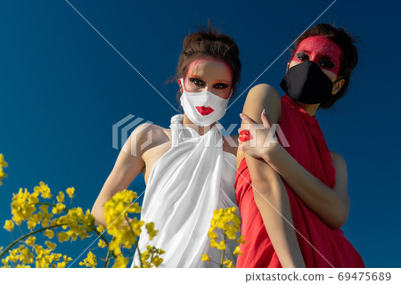 Two beautiful young brunette girls with creative bright makeup in tunics against a blue sky in a mask 69475689