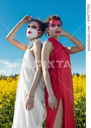 Two beautiful young brunette girls with creative bright makeup in tunics against a blue sky in a mask 69475708