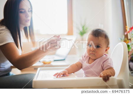 Funny adorable and dirty little baby girl of six months eats while sitting in the baby chair. 69476375