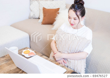 Young woman eating a snack while looking at a computer Young woman eating a snack while looking at a computer 69476527