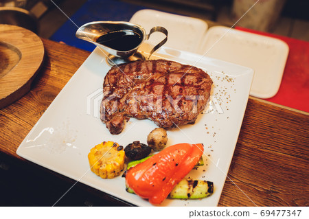 Beef grilled steak with set of grilled vegetables and glass of whiskey on wooden table close up beef. Beef grilled steak with set of grilled vegetables and glass of whiskey on wooden table close up beef. 69477347