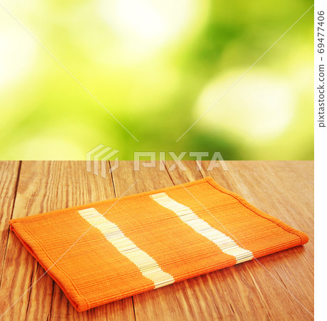 Orange bamboo placemat folded on wooden table against defocused background. Orange bamboo placemat folded on wooden table against defocused background. 69477406