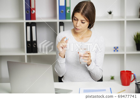 Young woman takes white round pill with glass of water in hand 69477741