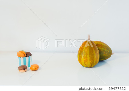 Minimalist Halloween concept - sweets, macarons dessert in a paper cup, and decorative pumpkins. Chocolate and pumpkin macaroons on a white background. Thanksgiving menu. Copy Space. Minimalist Halloween concept - sweets, macarons dessert in a paper cup, and decorative pumpkins. Chocolate and pumpkin macaroons on a white background. Thanksgiving menu. Copy Space. 69477812